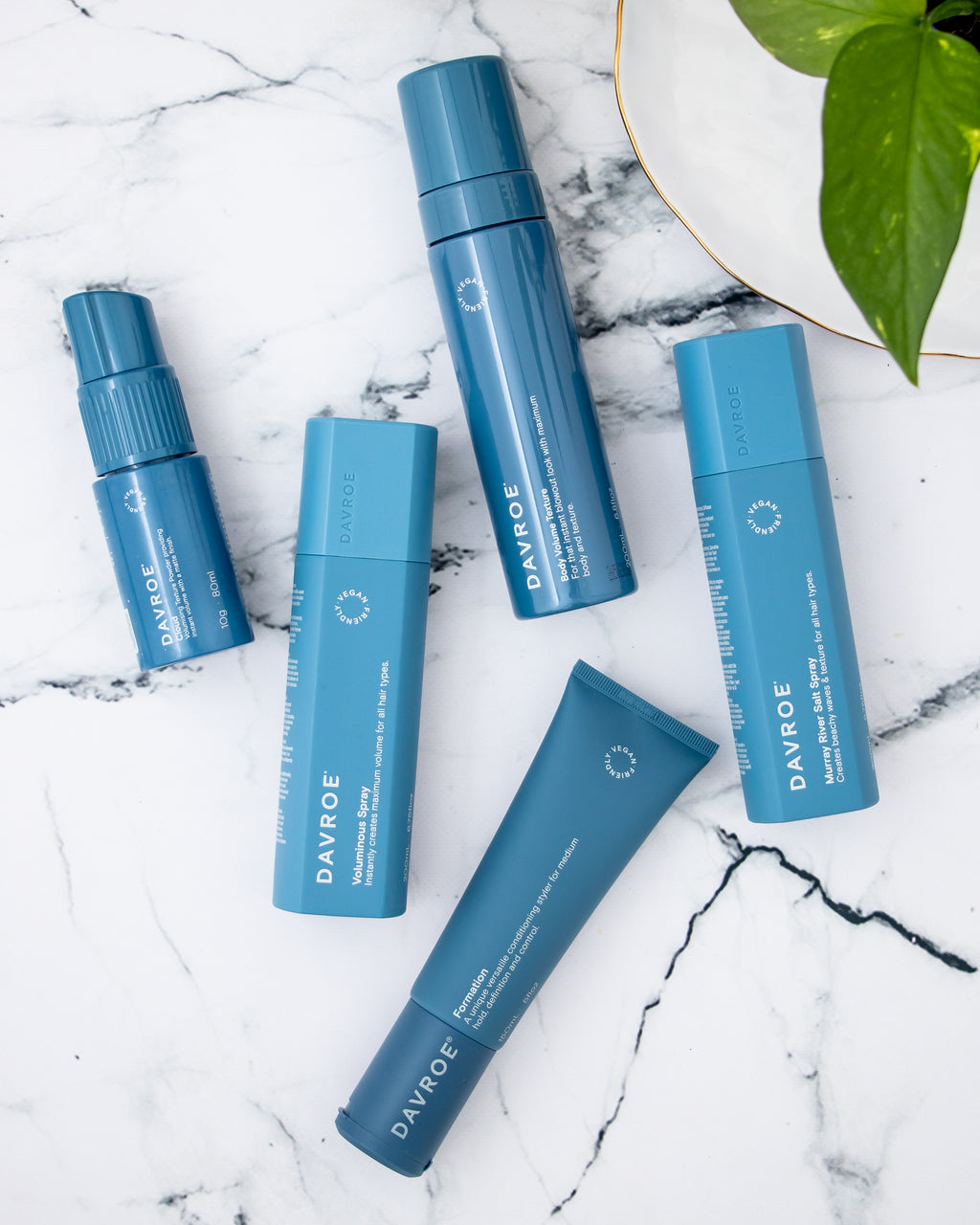 Set of blue Davroe hair care products on a marble surface with a plant leaf in the corner.