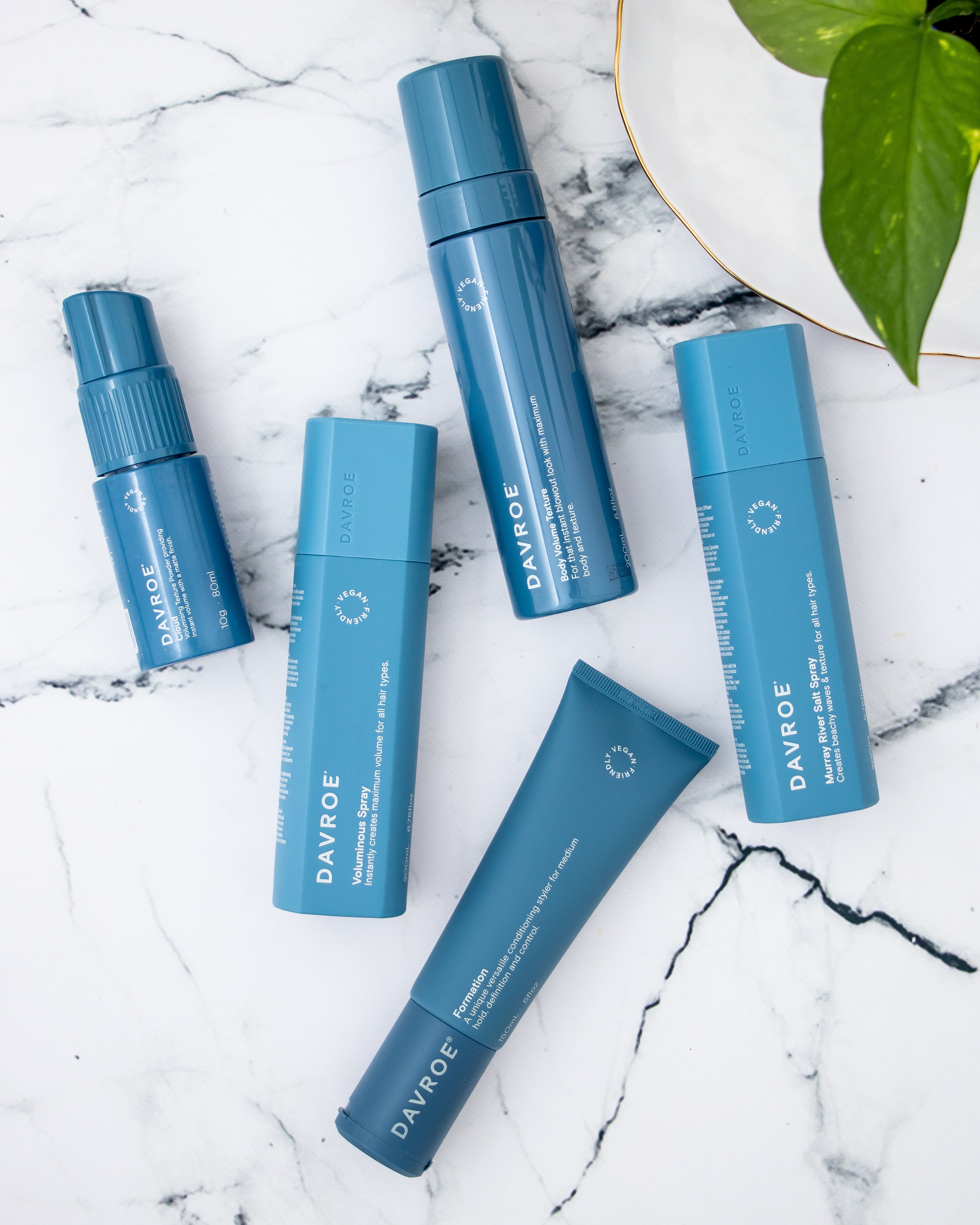 Set of blue Davroe hair care products on a marble surface with a plant leaf in the corner.