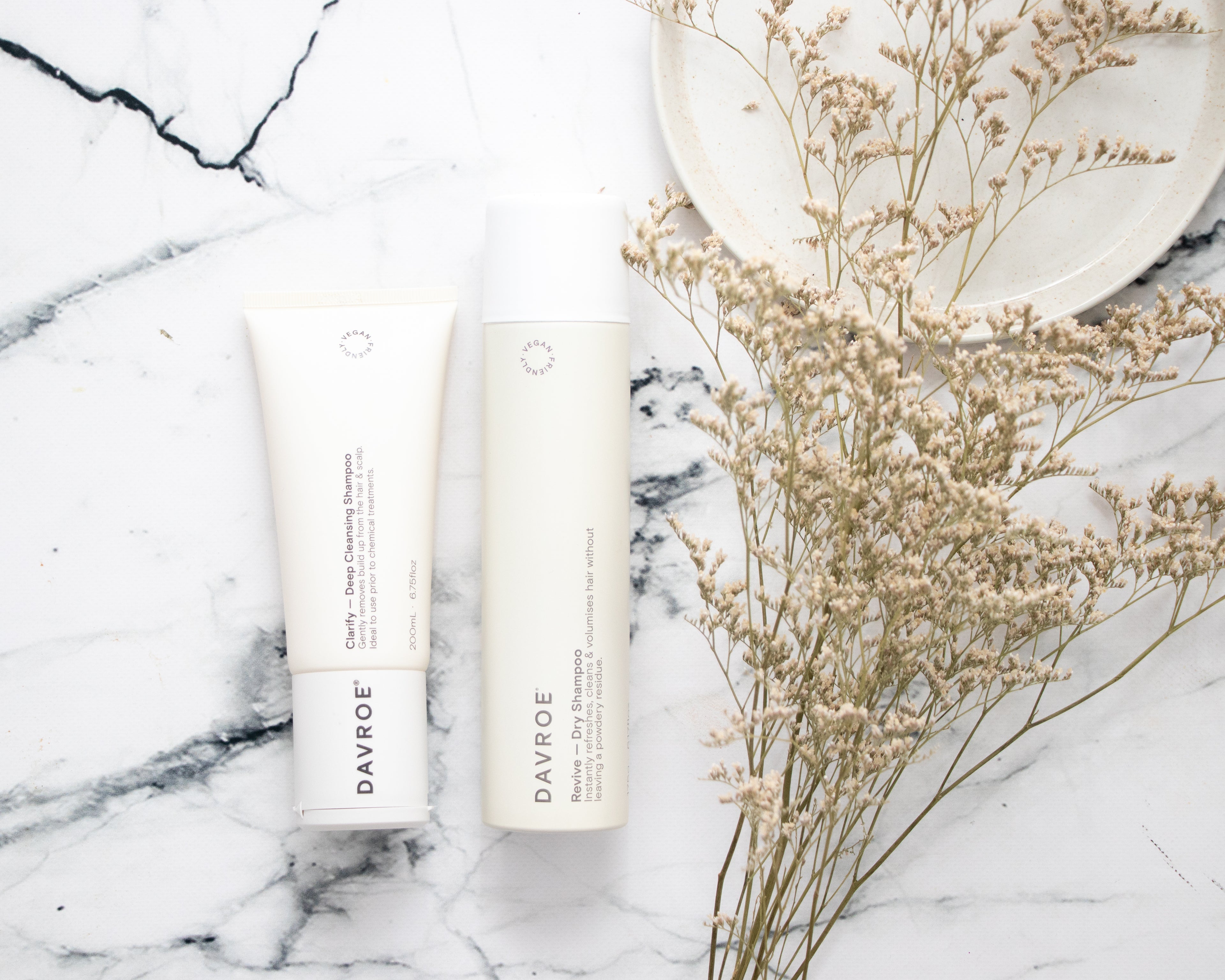 Two Davroe hair care products on a marble surface with dried flowers.